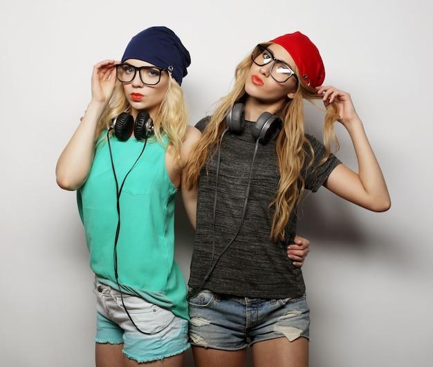 Studio styl życia portret dwóch najlepszych przyjaciółek hipsterskich dziewczyn w stylowych, jasnych strojach, kapeluszach, dżinsowych szortach i okularach, szalejących i świetnie się razem bawiących. Młoda i piękna.