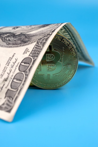 Studolarowy banknot i bitcoin na niebieskim tle