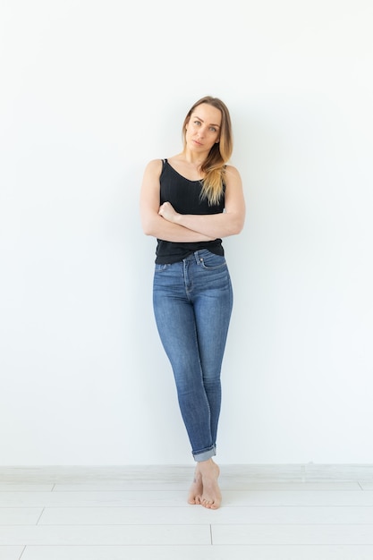 Styl, koncepcja ludzi - młoda kobieta w dżinsach i czarnej koszuli stojącej na białym tle