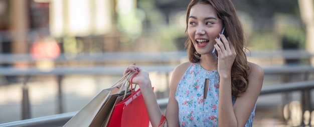 Styl życia kobiety młody szczęśliwy mienia torba na zakupy i opowiadać z przyjacielem na telefonie komórkowym z cieszyć się przy zakupy centrum handlowym.
