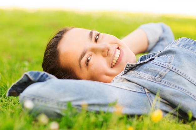 styl życia, letnie wakacje, wypoczynek i koncepcja ludzi - uśmiechnięta młoda dziewczyna leżąca na trawie