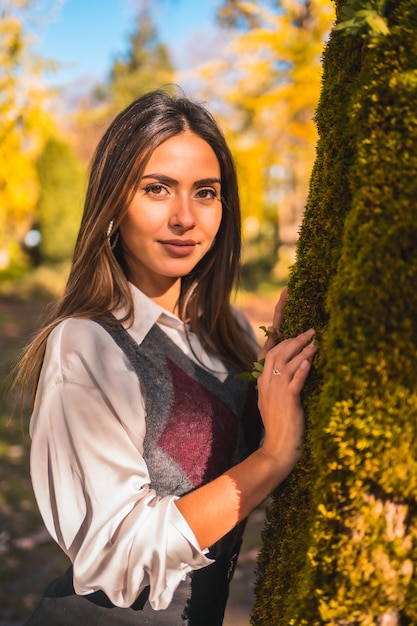 Styl życia, młoda brunetka, kaukaska studentka, pewnego jesiennego popołudnia w parku przy drzewie w modnej pozie