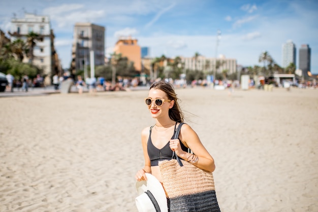 Styl życia portret ładnej kobiety w kapeluszu przeciwsłonecznym i torbie na plaży w Barcelonie