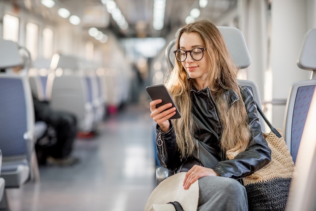 Styl życia portret młodej bizneswoman siedzącej ze smartfonem w nowoczesnym pociągu