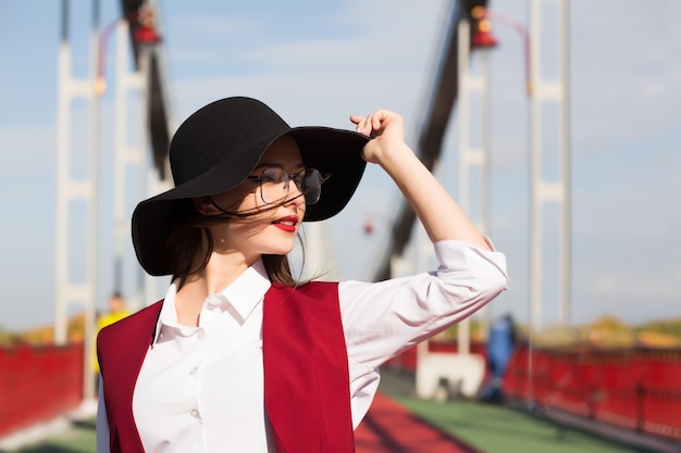 Styl życia portret piękny młody model pozowanie na moście. Kobieta w modnym kapeluszu, szaliku i okularach