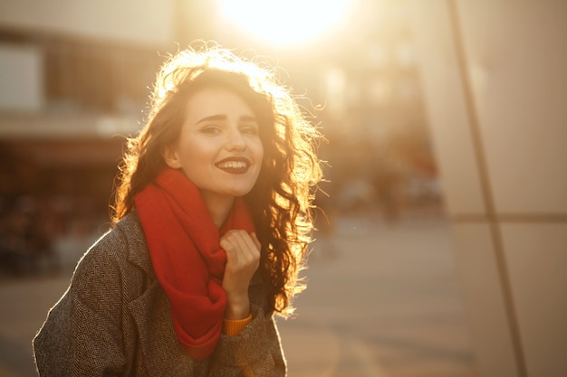 Styl życia portret radosny model brunetka z kręconymi włosami na sobie jesienny płaszcz oversize i czerwony szalik. Miejsce na tekst