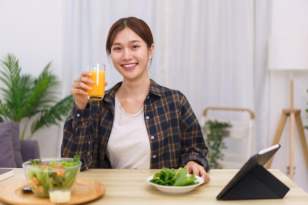 Styl życia w koncepcji salonu Azjatycka kobieta pijąca sok pomarańczowy i jedząca sałatkę jarzynową