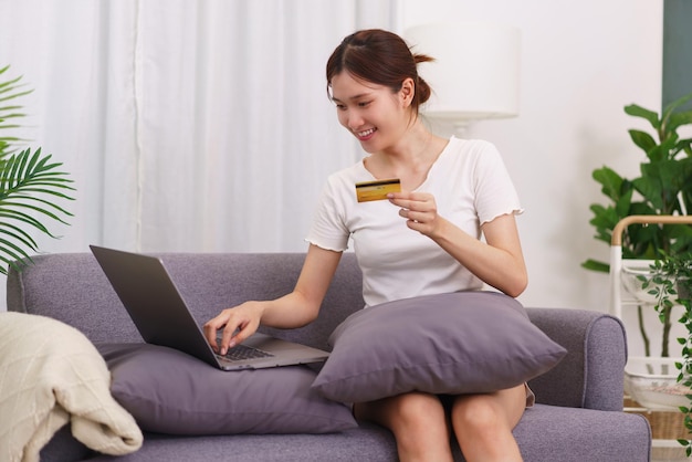 Styl życia w koncepcji salonu Azjatycka kobieta trzymająca kartę kredytową i używająca laptopa do zakupów online