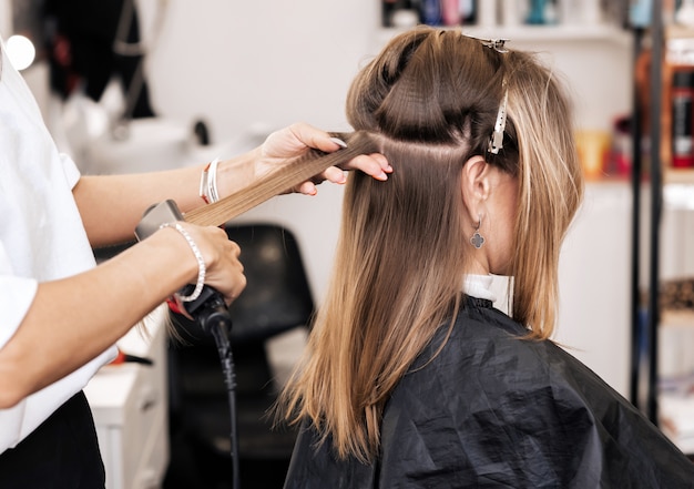 Zdjęcie stylista włosów tworzy objętość i stylizację dla brązowych włosów na głowie kobiety