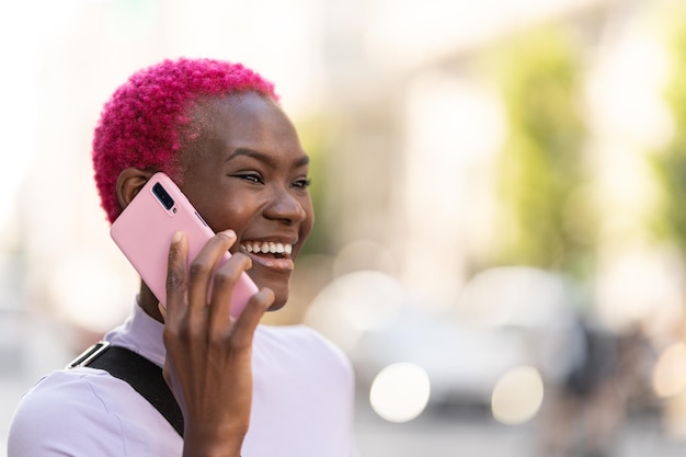 Stylowa afrykańska kobieta uśmiechająca się podczas rozmowy z telefonem komórkowym na zewnątrz