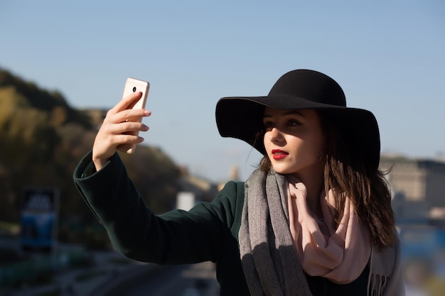 Stylowa brunetka dziewczyna turysta w kapeluszu robi zdjęcie selfie w słoneczny dzień w Kijowie