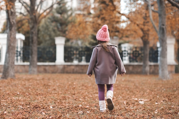 Stylowa dziecięca dziewczyna nosi dzianinową kurtkę z czapką spacer w parku na tle przyrody
