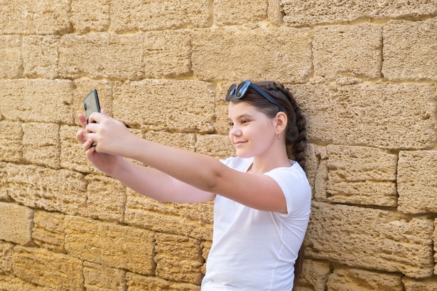 Stylowa dziewczyna nastolatek bierze selfie w mieście na kamiennym murem