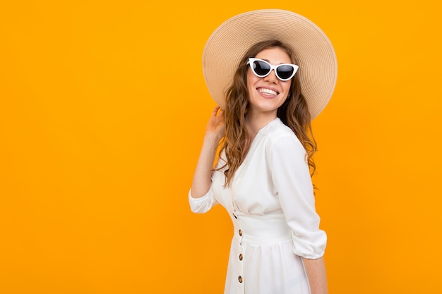 Stylowa dziewczyna w białym stroju i kapeluszu na tle pomarańczowej ściany
