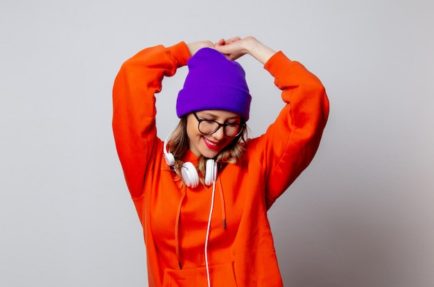 Stylowa dziewczyna w pomarańczowej bluzie i fioletowym kapeluszu ze słuchawkami