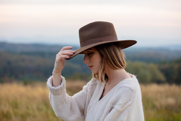 Zdjęcie stylowa dziewczyna w swetrze i kapeluszu na wsi z górami na tle