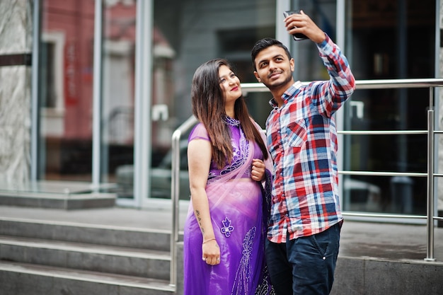 Stylowa indyjska para hinduska pozuje na ulicy i patrzy na telefon komórkowy i robi razem selfie