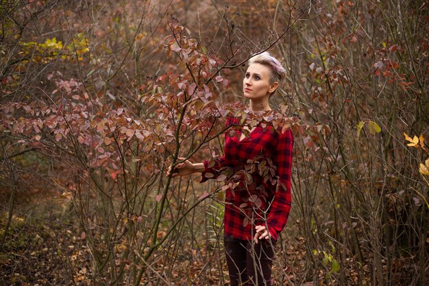 Stylowa kobieta hipster z krótką fryzurą w jesiennym tle z uschniętymi jesiennymi drzewami