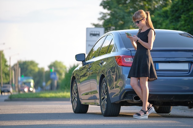 Stylowa kobieta kierowca stojący w pobliżu swojego pojazdu, rozmawiający przez telefon komórkowy na ulicy miasta w lecie