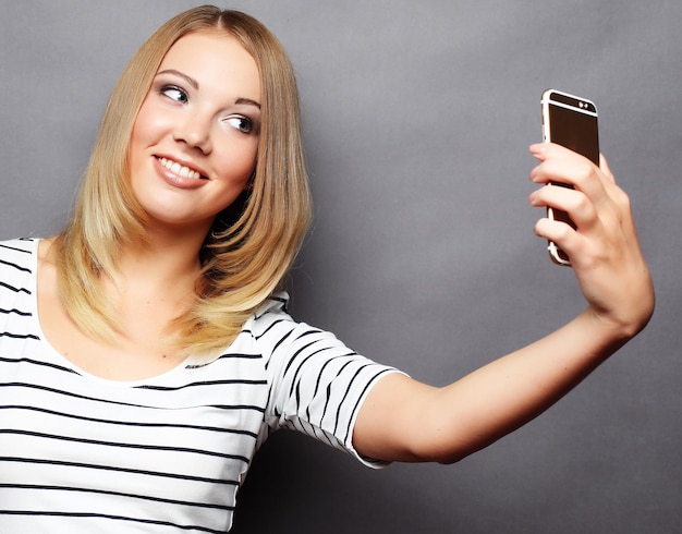 Stylowa kobieta robi zdjęcie selfie na smartfonie na szarym tle