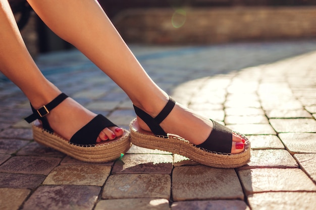 Stylowa kobieta ubrana w czarne letnie buty ze słomy podeszwa na zewnątrz. Wygodne sandały. Moda uroda.