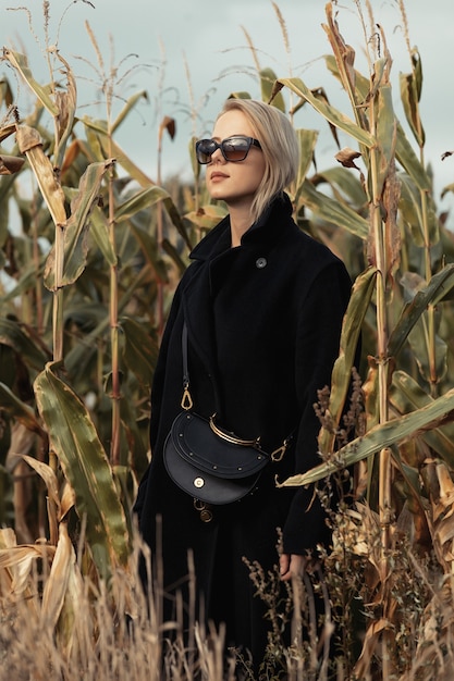 Zdjęcie stylowa kobieta w czarnym płaszczu w jesiennym polu kukurydzy