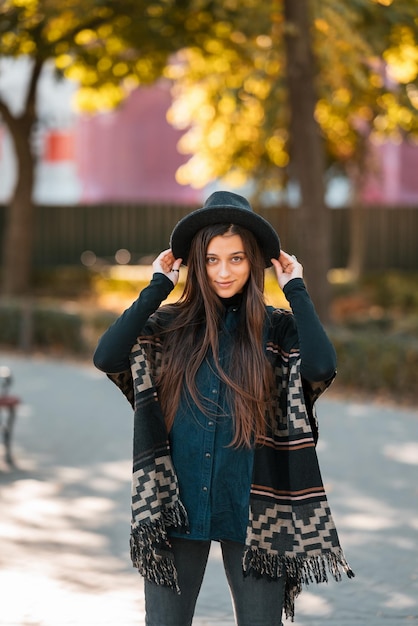 Stylowa kobieta w ponczo i kapeluszu cieszy się jesiennym parkiem
