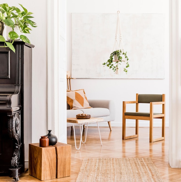 Stylowa kompozycja kreatywnego, przestronnego wnętrza mieszkania z szarą sofą, krzesłem, stolikiem kawowym, roślinami, dywanem i pięknymi dodatkami. Białe ściany i parkiet.