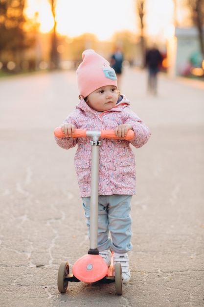 Stylowa mała dziewczynka jedzie hulajnoga w parku przy zmierzchem