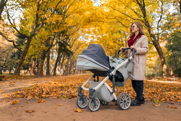 Stylowa mama z wózkiem w jesiennym parku