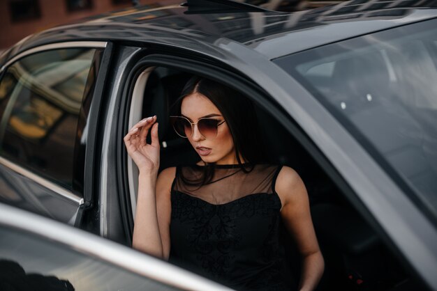 Stylowa młoda dziewczyna siedzi w samochodzie klasy biznes w czarnej sukience. Biznesowa moda i styl
