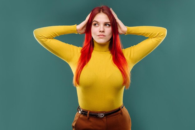 Stylowa młoda kobieta z długimi rudymi włosami ubrana w żółty sweter pozuje emocjonalnie na tle studia