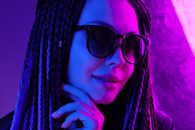 Stylowa młoda kobieta z warkoczami w okularach przeciwsłonecznych na fioletowym tle