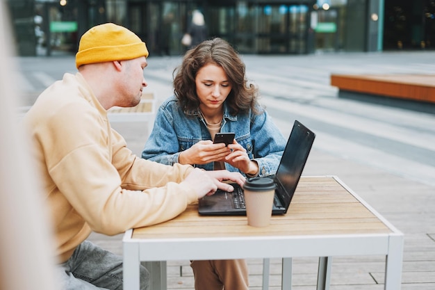 Stylowa młoda para freelancerów pracujących na laptopie w ulicznej kawiarni