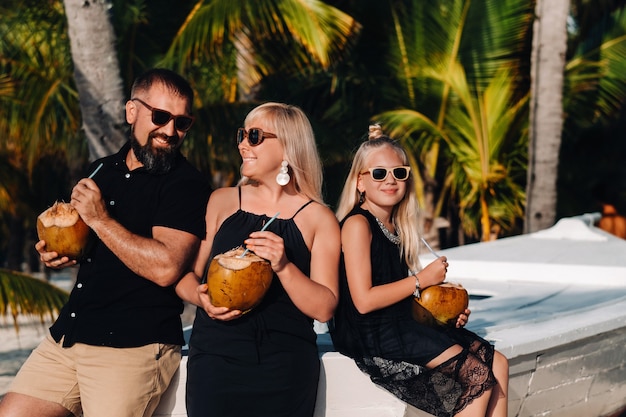 Stylowa rodzina w czarnych ubraniach z kokosami w dłoniach na plaży wyspy Mauritius. Piękna rodzina na wyspie Mauritius na Oceanie Indyjskim.