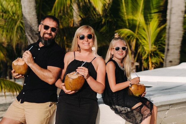 Stylowa rodzina w czarnych ubraniach z kokosami w dłoniach na plaży wyspy MauritiusPiękna rodzina na wyspie Mauritius na Oceanie Indyjskim