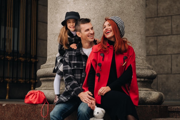 Stylowa trzyosobowa rodzina przechadza się po jesiennym mieście pozując dla fotografa Tata mama i córka w jesiennym mieście