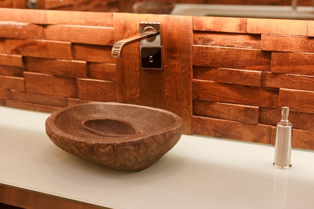 Stylowa umywalka wykonana z jasnego kamienia naturalnego. Łazienka z kamienną umywalką na drewnianym blacie w stylu tropikalnego loftu.