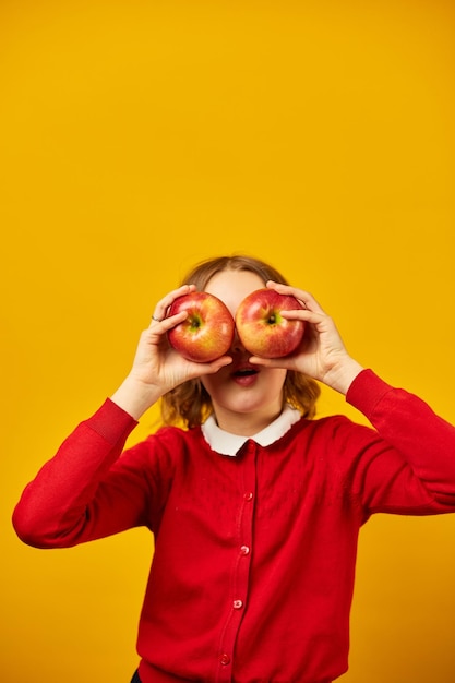 Stylowa uśmiechnięta szkolna nastolatka trzymająca jabłka przed oczami na żółtym tle studia powrót do koncepcji zdrowia oczu szkoły