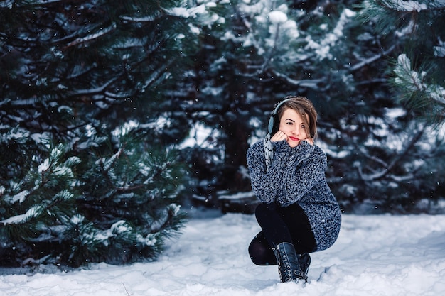 Stylowa wesoła dziewczyna w swetrze w zimowym lesie