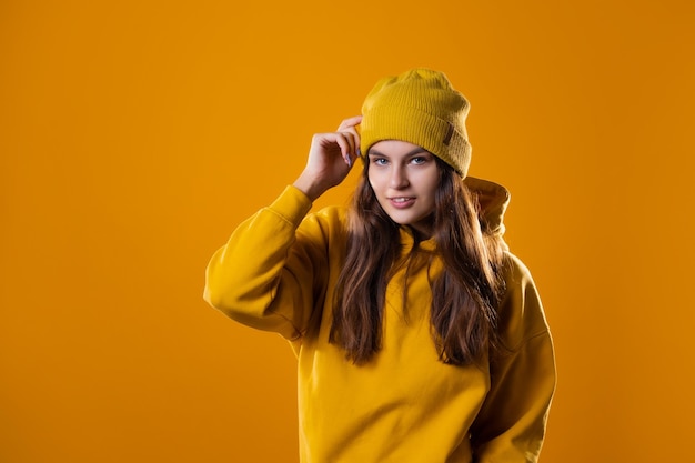 Stylowa wesoła młoda brunetka w żółtej bluzie z kapturem i kapeluszu na żółtym tle