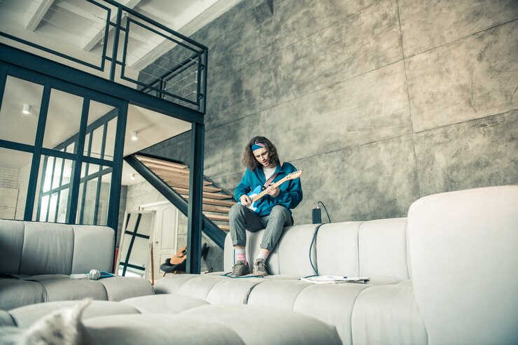 Stylowe apartamenty. Długo zatrudniony, utalentowany facet siedzi na kanapie, ćwicząc swoje umiejętności w profesjonalnym występie na gitarze