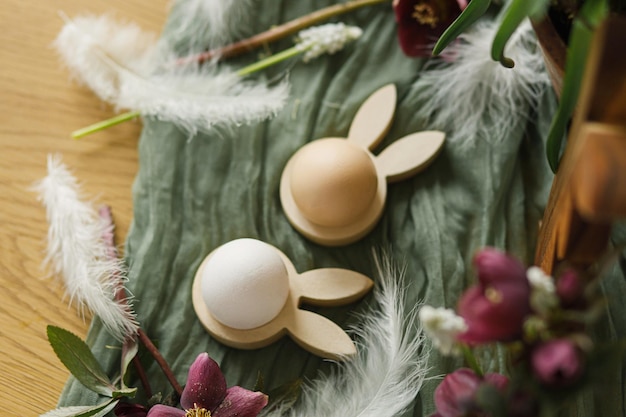Stylowe drewniane uszy królika i naturalne jajka wiosenne kwiaty pióra i gniazdo na rustykalnym stole z bliska Wesołych Świąt Wielkanocna martwa natura Świąteczna aranżacja i wystrój w wiejskim widoku z góry