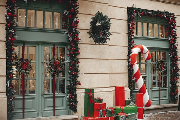 Stylowe duże cukierki trzciny cukrowej czerwone i zielone zawinięte prezenty świąteczne wieńce z gałęzi jodłowych na zewnątrz budynku Nowoczesny wystrój świąteczny na ulicy miasta Zimowe wakacje w Europie