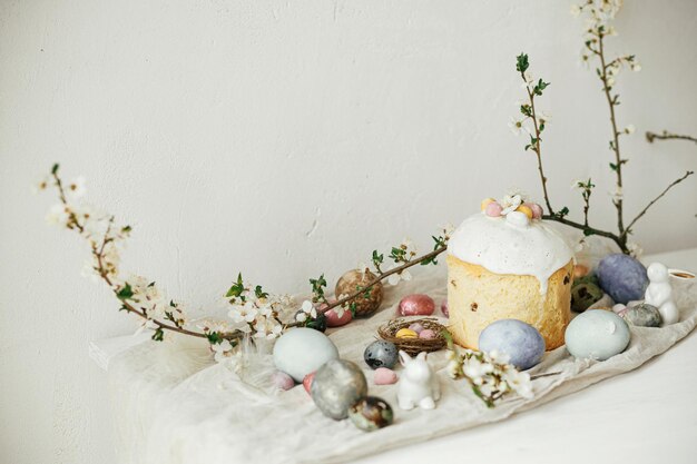 Stylowe jaja wielkanocne króliczki panettone kompozycja kwiatów wiśni na rustykalnym stole Szczęśliwa Wielkanoc Nowoczesne naturalne farbowane jaja świąteczne jedzenie i wiosenne kwiaty Wiejska martwa natura