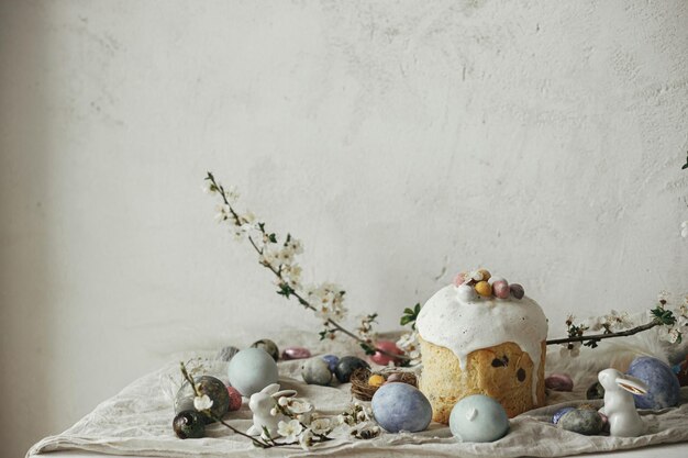 Stylowe jaja wielkanocne króliczki panettone kompozycja kwiatów wiśni na rustykalnym stole Szczęśliwa Wielkanoc Nowoczesne naturalne farbowane jaja świąteczne jedzenie i wiosenne kwiaty Wiejska martwa natura