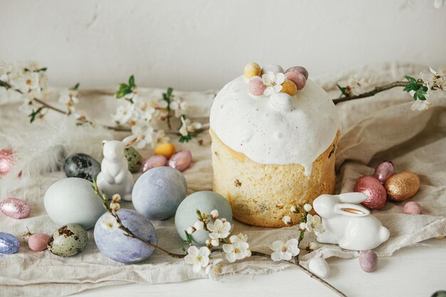 Stylowe jaja wielkanocne króliczki panettone kompozycja kwiatów wiśni na rustykalnym stole Szczęśliwa Wielkanoc Nowoczesne naturalne farbowane jaja świąteczne jedzenie i wiosenne kwiaty wiejskie martwe życie