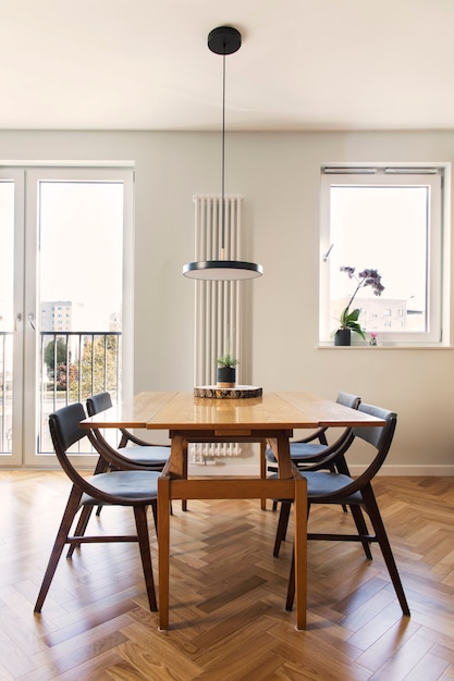 Stylowe skandynawskie wnętrze jadalni z rodzinnym stołem i krzesłami oraz akcesoriami. Jasny, przestronny i słoneczny pokój z dużymi oknami i brązowym drewnianym parkietem.
