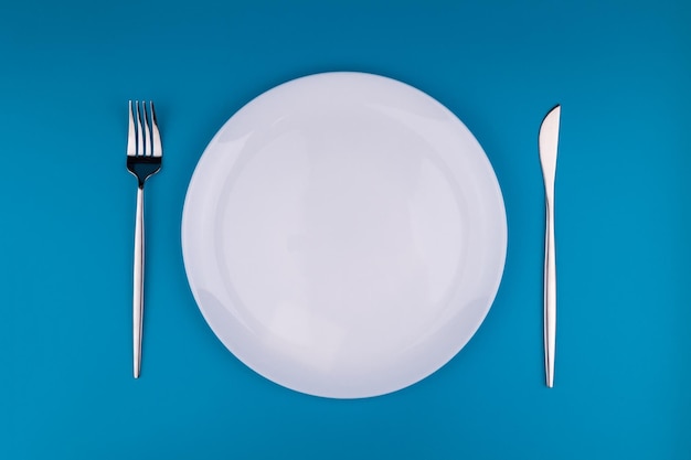 Stylowe ustawienie stołu pusta biała płyta z widelcem i nożem na niebieskim tle widok z góry płaska lay