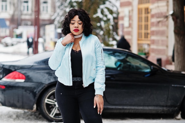 Stylowy afroamerykanin plus size model z telefonem komórkowym pod ręką w zimowy śnieżny dzień na czarnym samochodzie